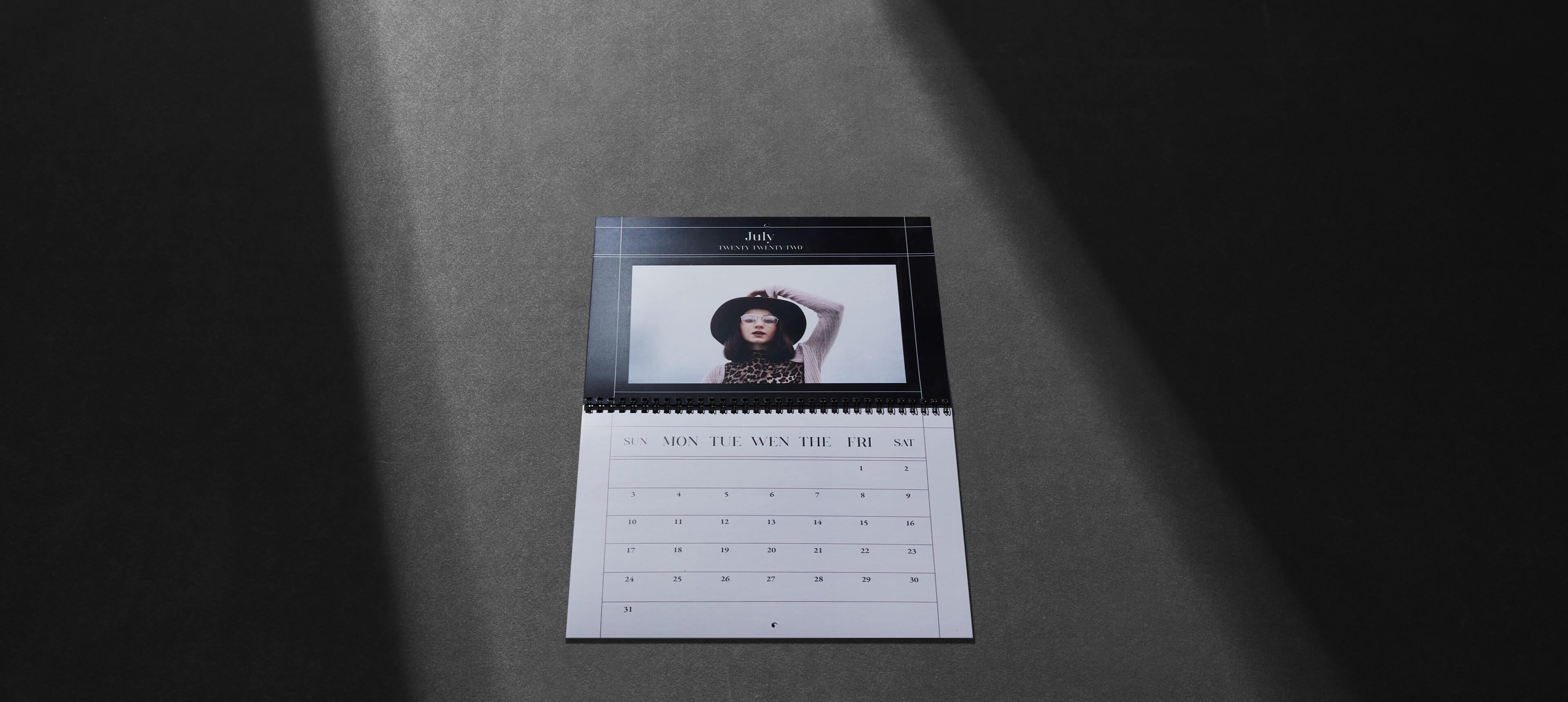 a classic wall calendar on a grey table showing a woman wearing a hat