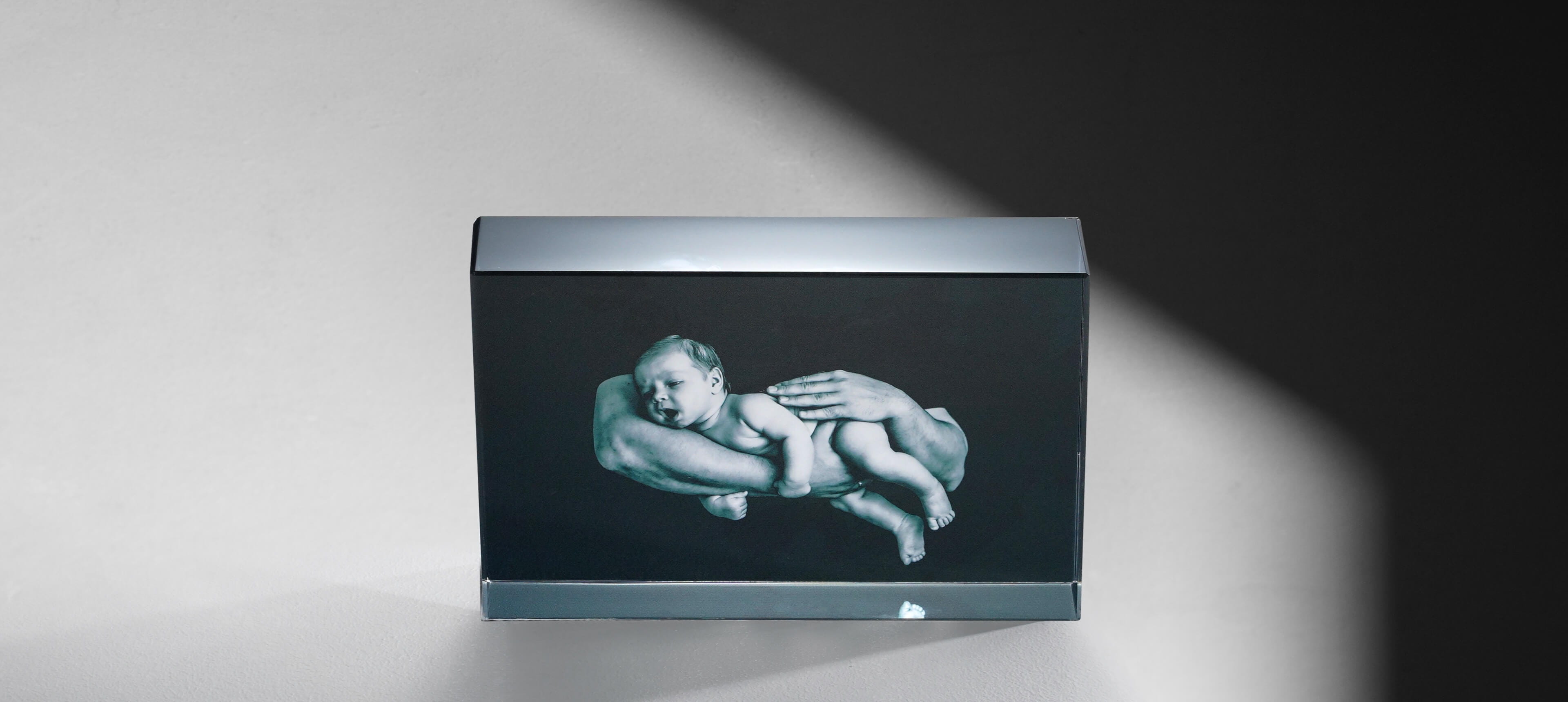 a crystal glass photo block stands on white table showing a baby in arms