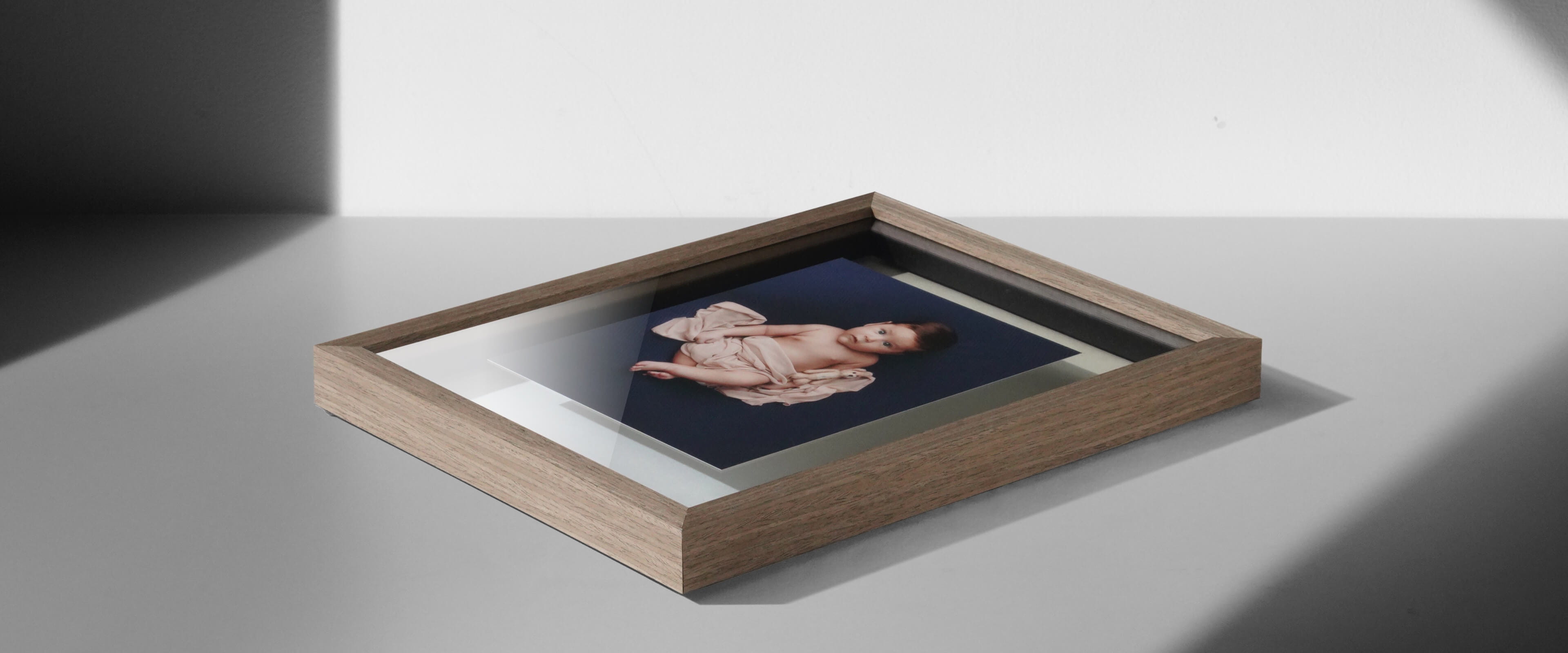 double glass frame with light brown wood frame and photo of baby laying on table
