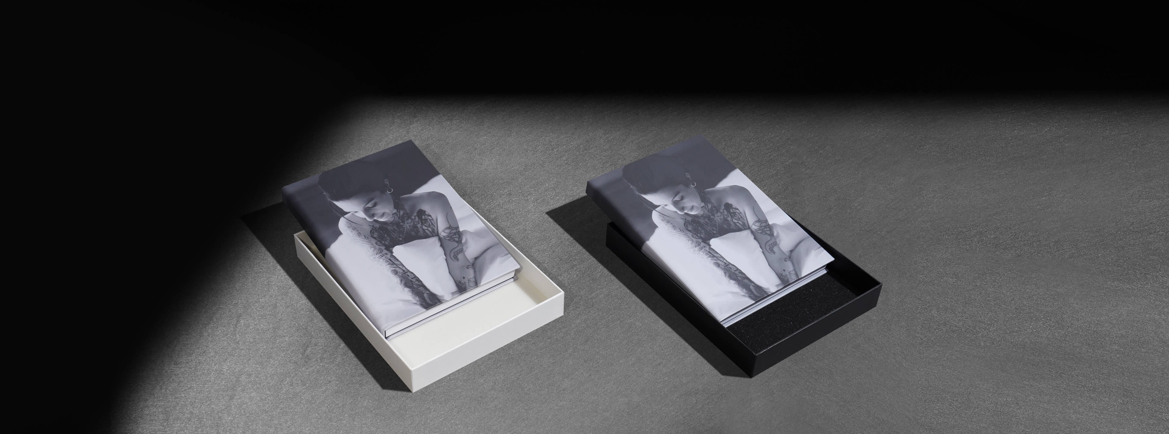 a black box and a white box that each hold the same boudoir photo album showing a semi nude woman