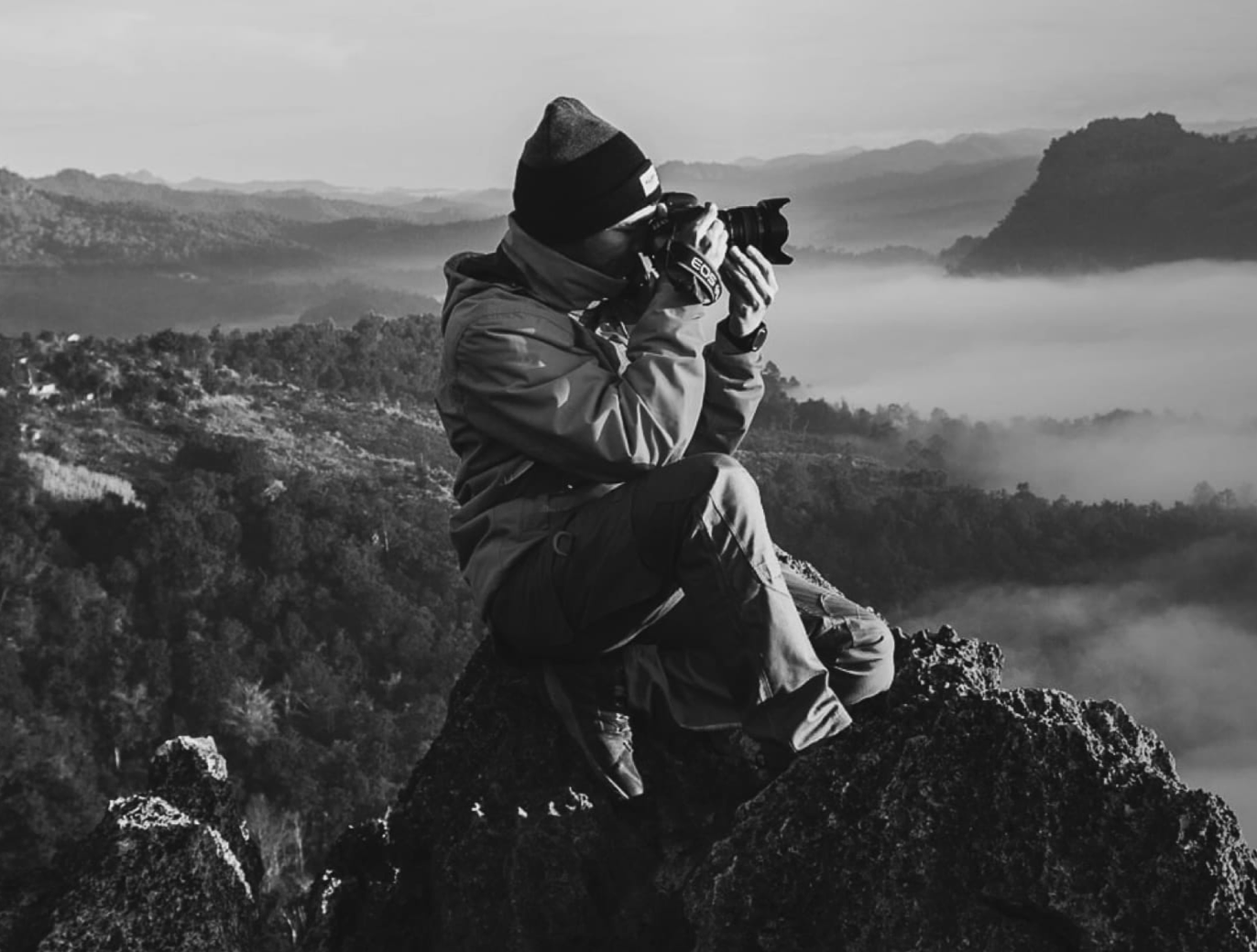 man capturing a photo while seated on a rock