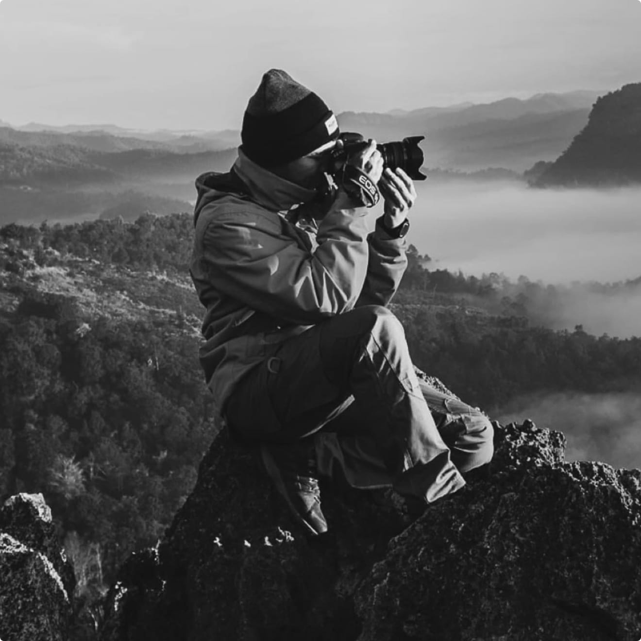 man capturing a photo while seated on a rock