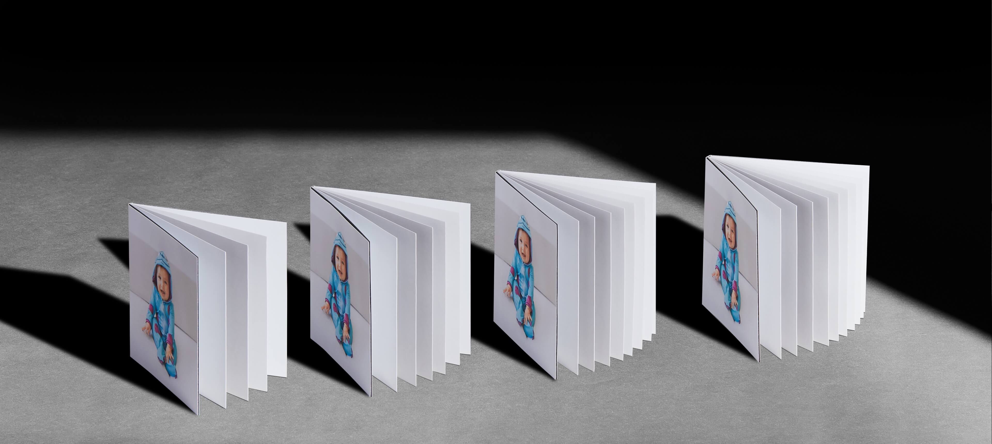 four layflat booklets standing on a grey table showing different page options