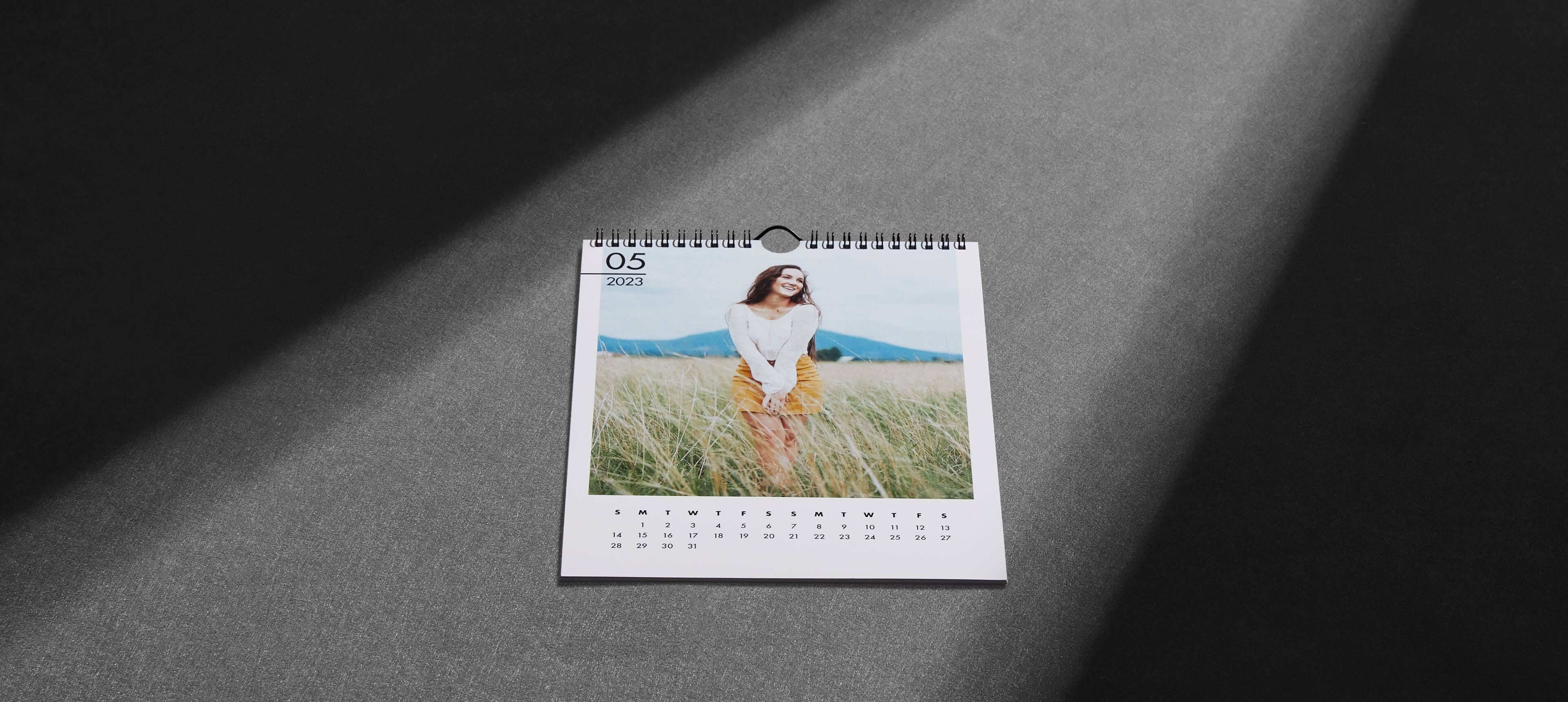 a modern wall calendar on a grey table showing a woman in a field