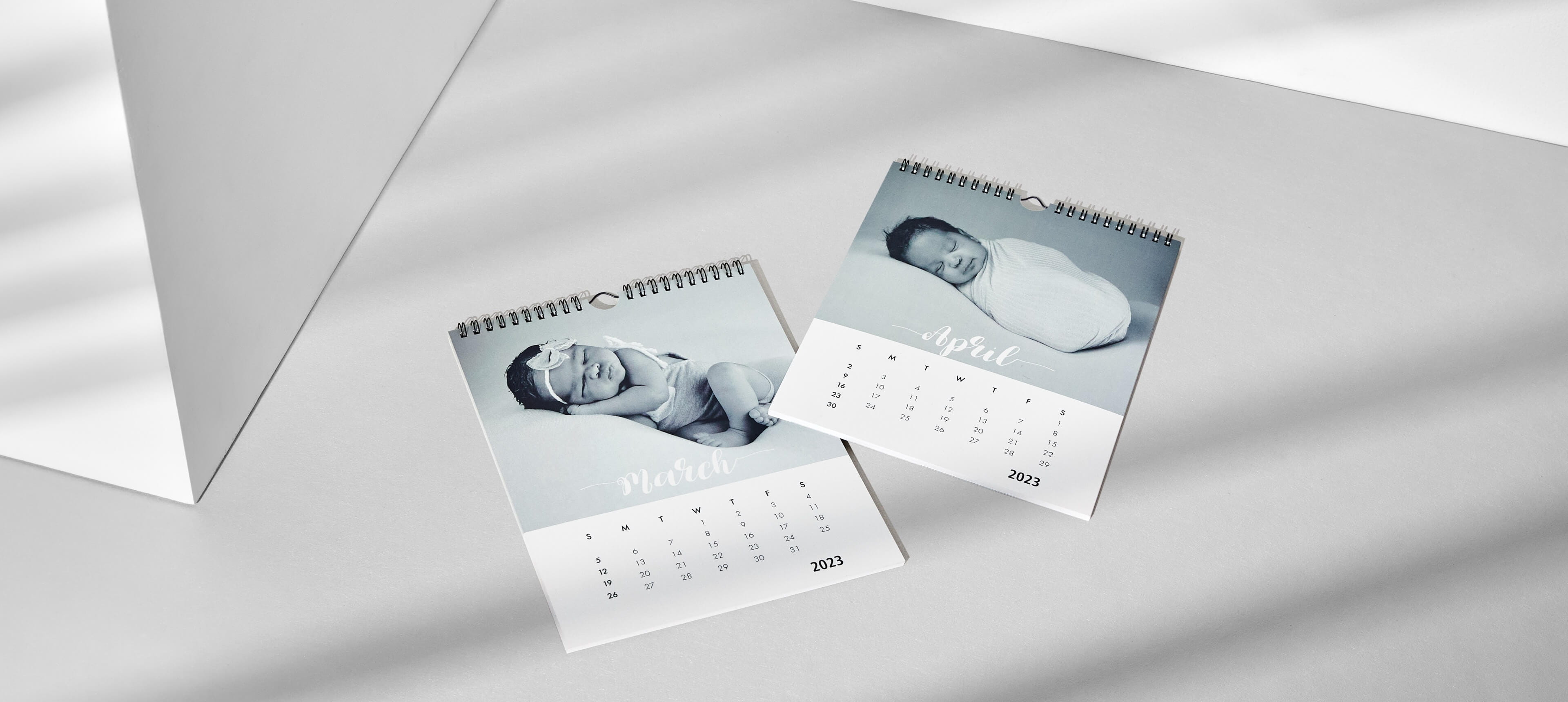 two modern wall calendars on a white table showing a baby sleeping