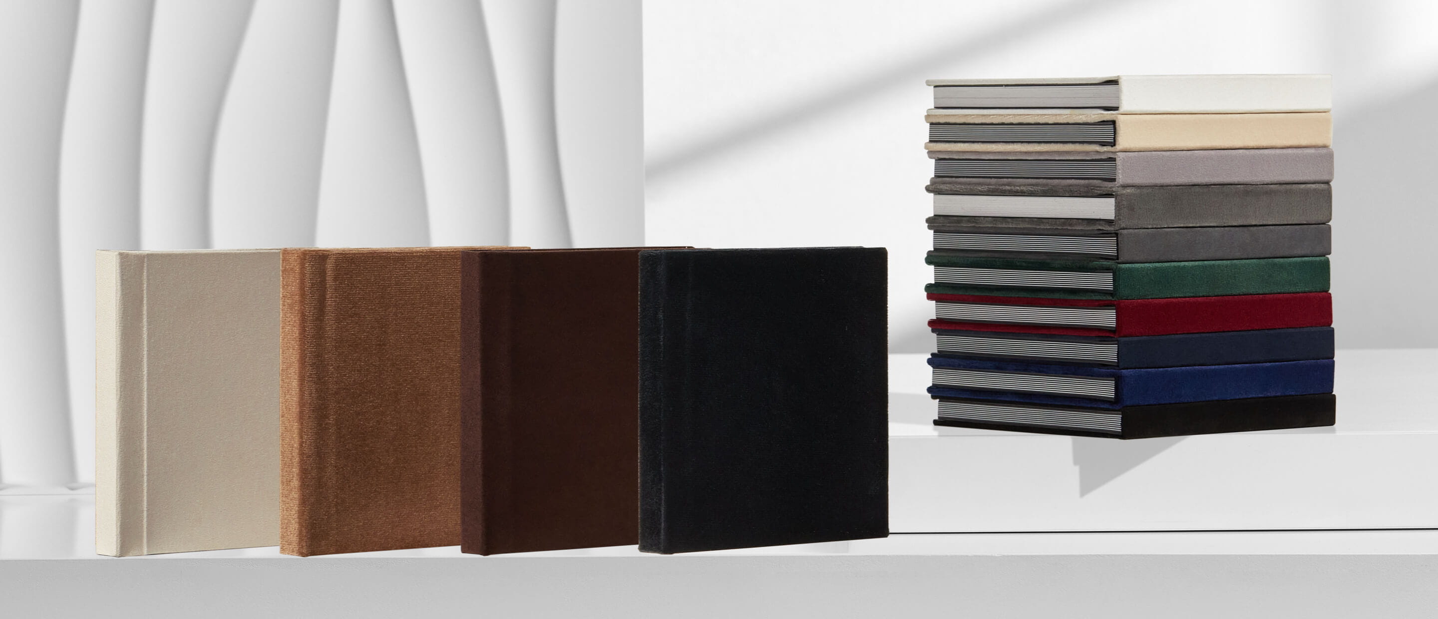 fourteen suede and velvet albums in different colors on a white table